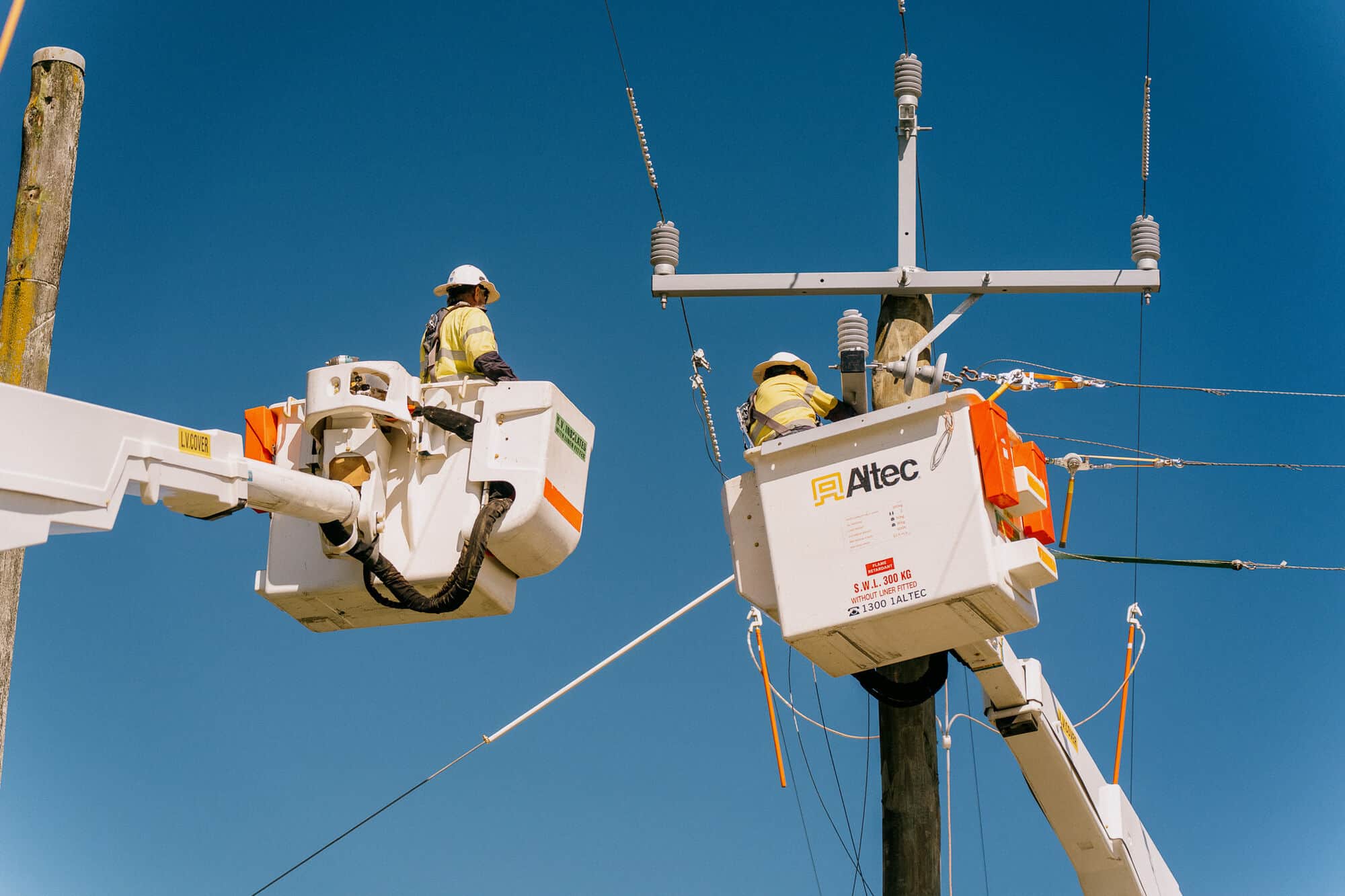 Two bucket trucks working on a power pole against deep blue sky