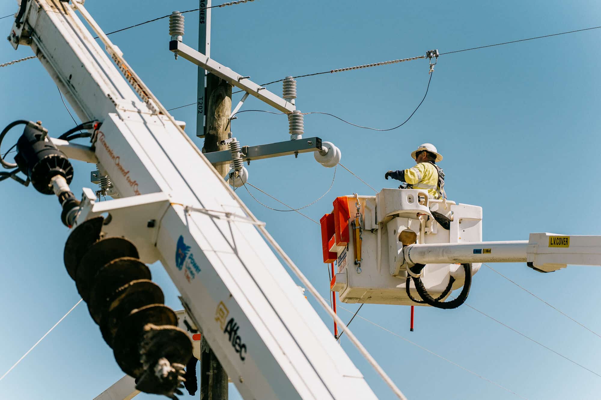 Lineman in a bucket truck beside an auger crane on a power pole